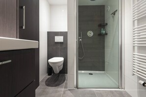 Een moderne badkamer met een douchecabine van glas, een toilet en donkere kastjes.