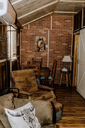 A rustic barn-style room with wooden furniture, a brick wall, and a horse painting.