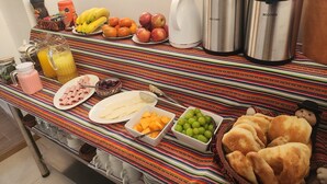 A breakfast buffet with various fruits, pastries, and beverages on a colorful striped tablecloth. - INCA PALACE EXPERIENCE (Puno)