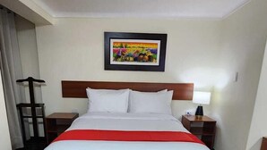 A hotel room with a large bed, a wooden parquet floor, a nightstand with a lamp, and a painting on the wall. - INCA PALACE EXPERIENCE (Puno)