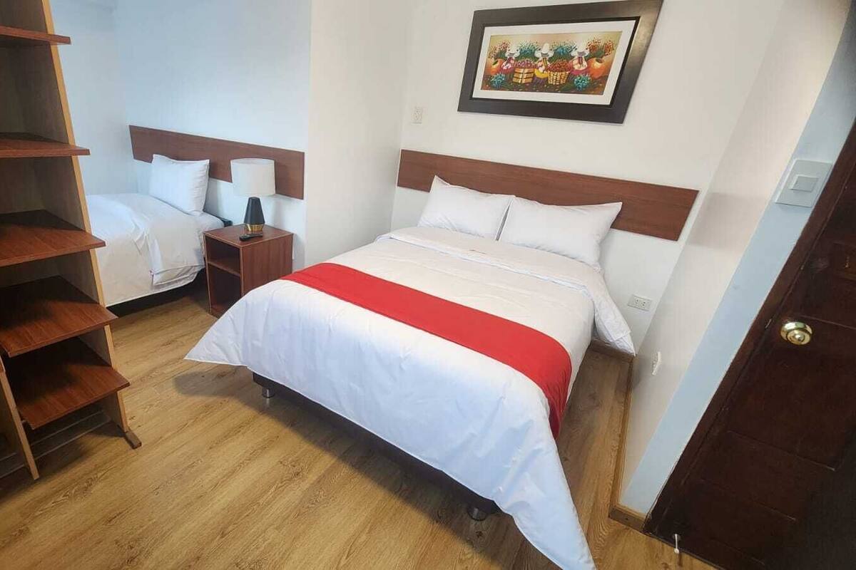 A bedroom with a bed, a nightstand, a wooden wardrobe, and a painting on the wall.