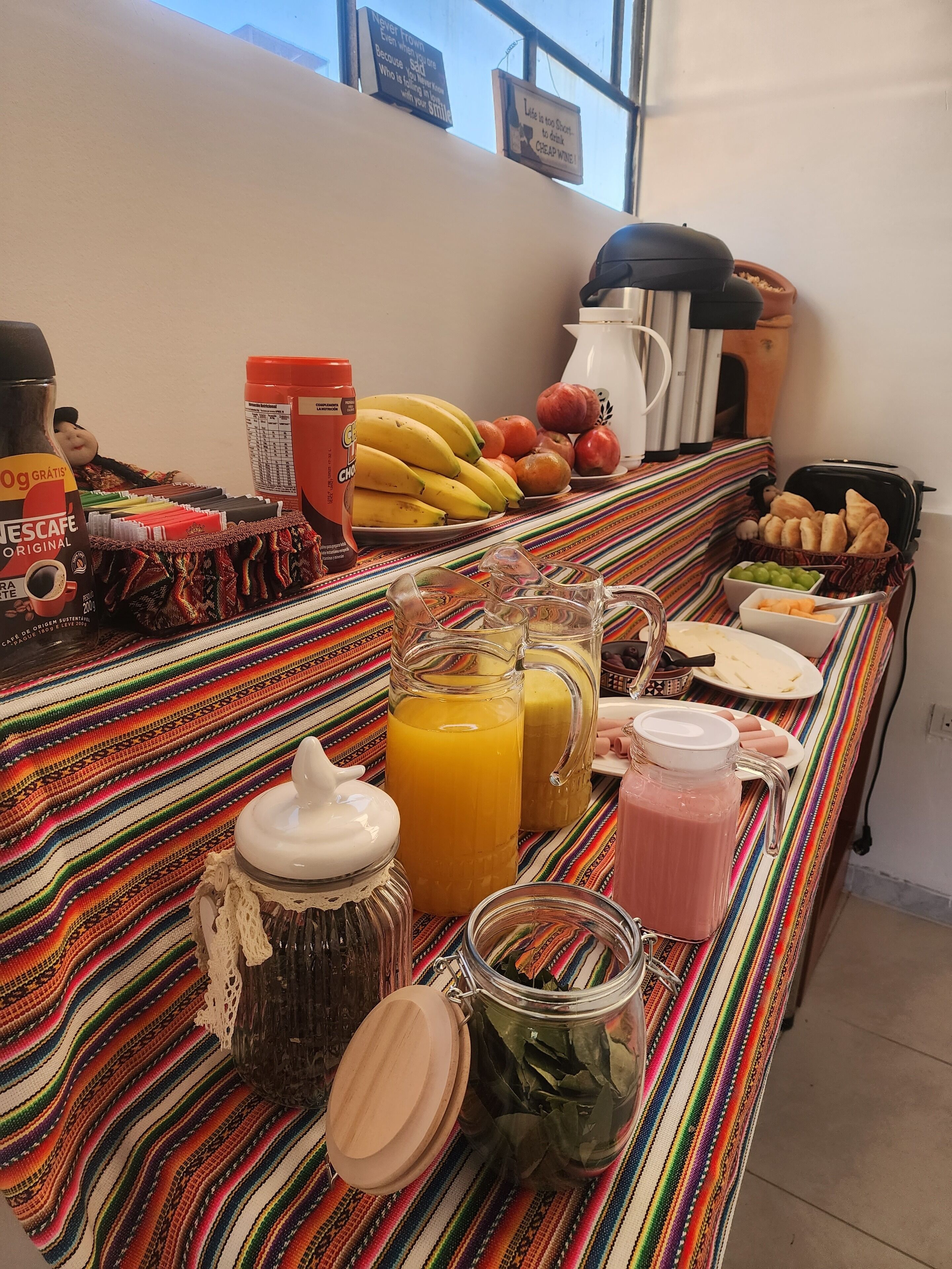 Un buffet de petit-déjeuner proposant une grande variété d’aliments et de boissons, notamment des fruits, du pain et diverses boissons, disposés sur une nappe rayée aux couleurs vives.