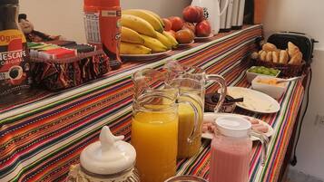 Un buffet de petit-déjeuner proposant une grande variété d’aliments et de boissons, notamment des fruits, du pain et diverses boissons, disposés sur une nappe rayée aux couleurs vives.