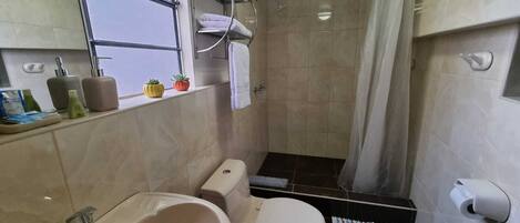Casa de banho com banheira, sanita e chuveiro. Toalhas e artigos de higiene pessoal estão na bancada.