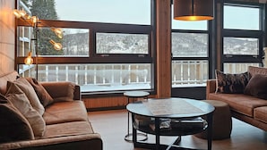 Un salon chaleureux avec un canapé en cuir marron, une table basse ronde et une vue sur un paysage enneigé, visible à travers de grandes fenêtres.