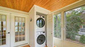 A laundry room with a stacked washer and dryer, wooden flooring, and a large window with a view of a residential area.