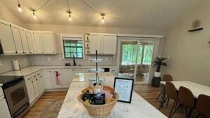 A spacious kitchen with white cabinets, a marble island, and a dining area with brown chairs.