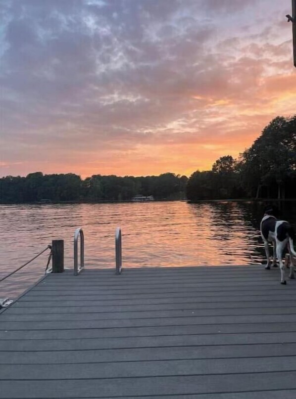 A wooden dock extending into a calm body of water with a sunset in the background.