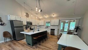 A modern kitchen with a central island, white cabinets, and a dining area with a long table and bar stools.