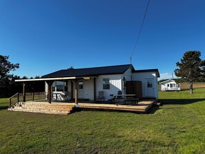 A single-story house with a covered porch, a small deck, and a fenced yard. - Looking for a Cozy, Comfortable Cottage on the beautiful south shore of PEI? (Victoria)