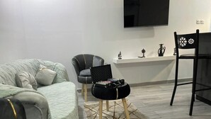 Ein modernes Wohnzimmer mit grauem Sofa, einem schwarzen Sessel, einem kleinen schwarzen Hocker und einem schwarzen Stuhl, sowie einem an der Wand befestigten Flachbildfernseher.