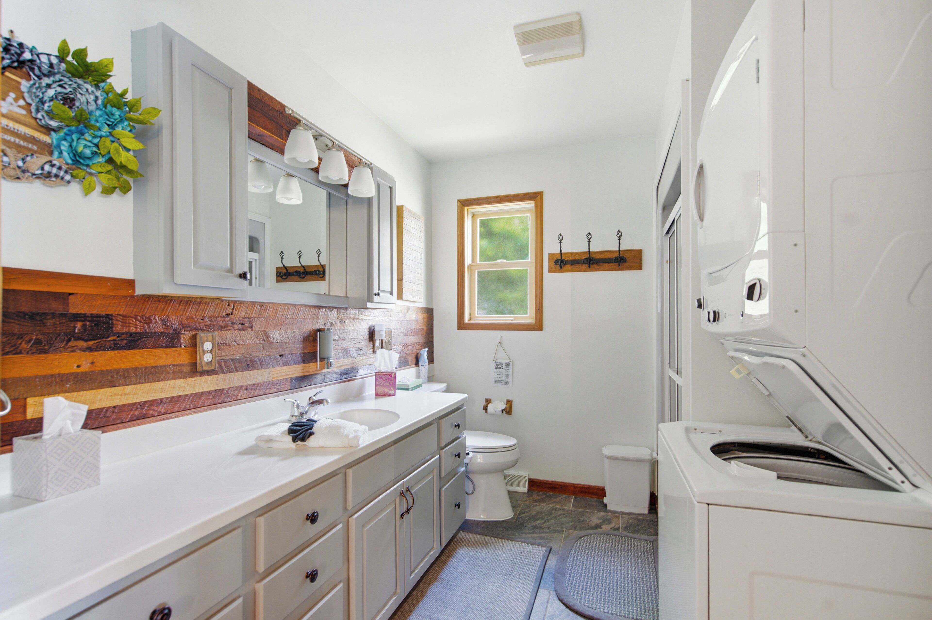 Un baño con una pared de acento de madera, un espejo grande, un lavamanos, un inodoro y una lavadora.
