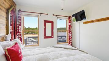 A bedroom with a bed, a TV mounted on the wall, and a view of the outdoors through the windows.