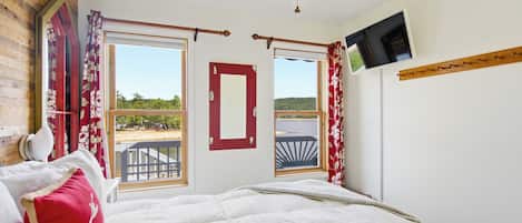 A bedroom with a bed, a TV mounted on the wall, and a view of the outdoors through the windows.