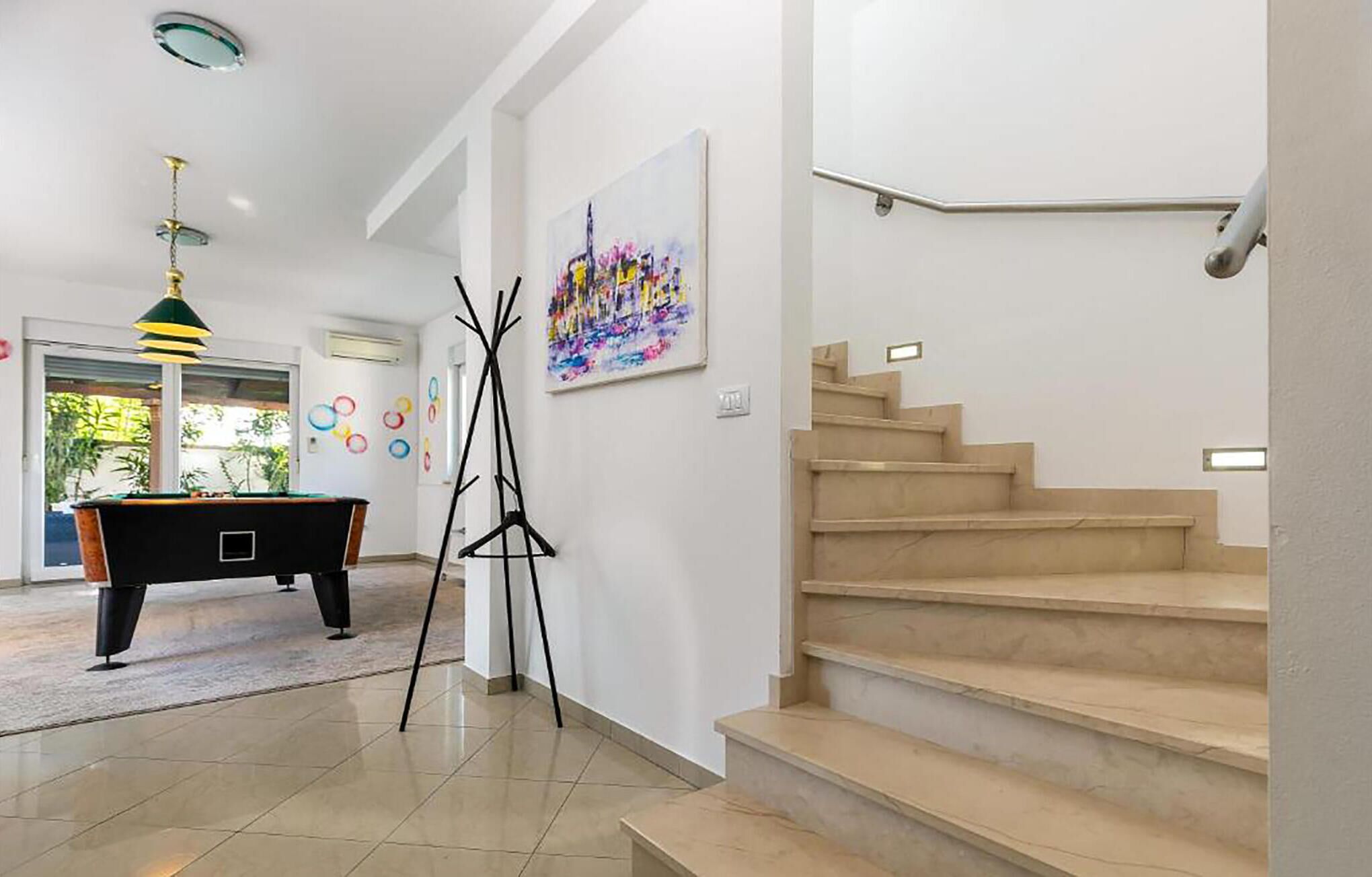 A spacious room with a pool table, a staircase, and a painting on the wall.