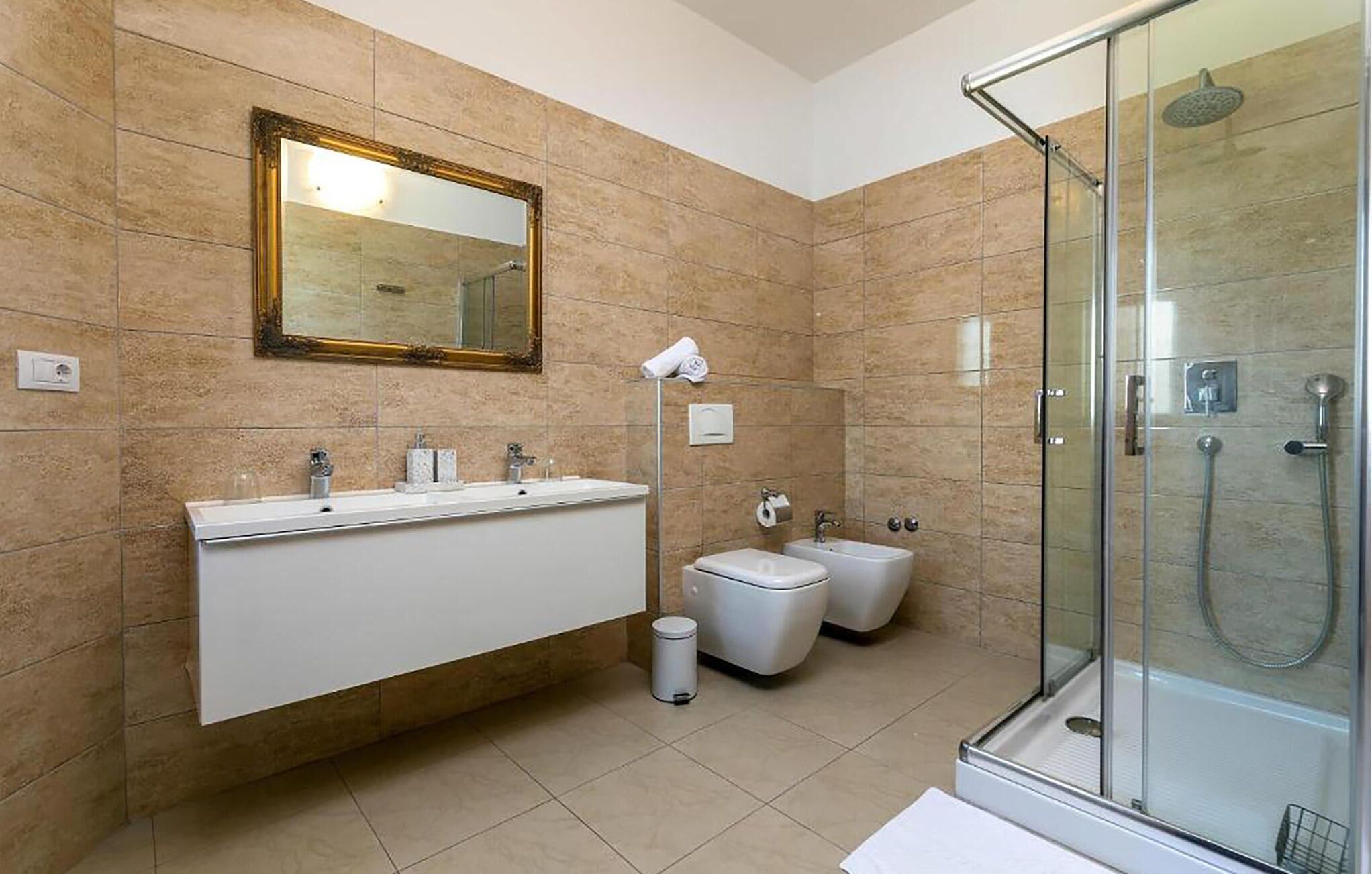 A modern bathroom with a large mirror, a double sink vanity, a toilet, a bidet, and a glass-enclosed shower area.