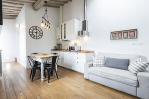 Una cocina moderna con armarios blancos, una mesa de comedor con sillas, un sofá blanco y un reloj de pared.
