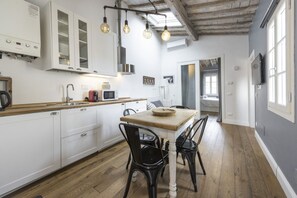 A kitchen with white cabinets, a wooden countertop, a dining table with black chairs, and hanging light fixtures. - Central Nest by MMega (Firenze)