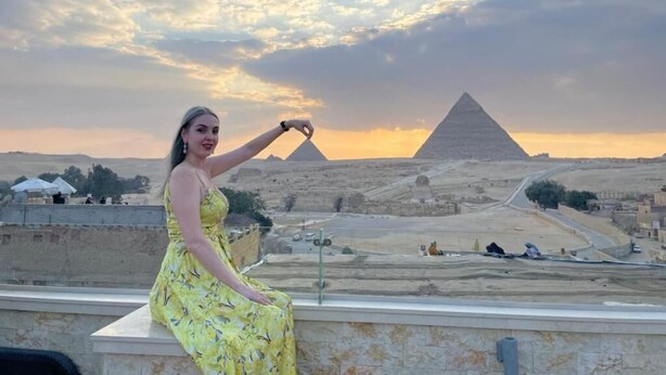 En person i en gul klänning sitter på en balkong med utsikt över pyramiderna.