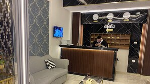 En hotellobby med en soffa, ett soffbord i glas och en receptionsdisk.