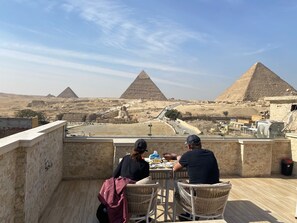 A rooftop terrace with a view of the pyramids, featuring a table and chairs for dining. - Rehana Pyramids View (Giza)