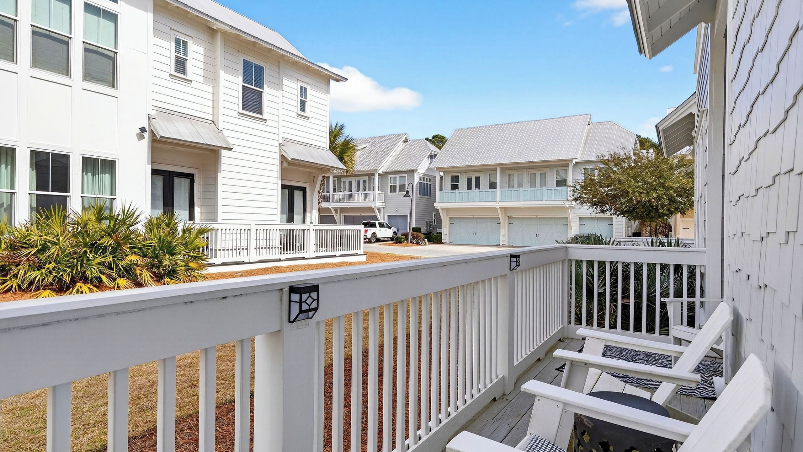 A residential area with white houses, a wooden deck, and a clear sky.