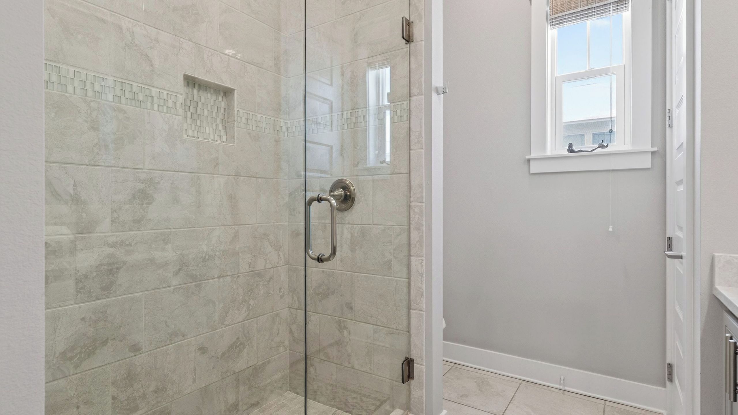 Eine Dusche mit Glastür, Handlauf und Fenster darüber.