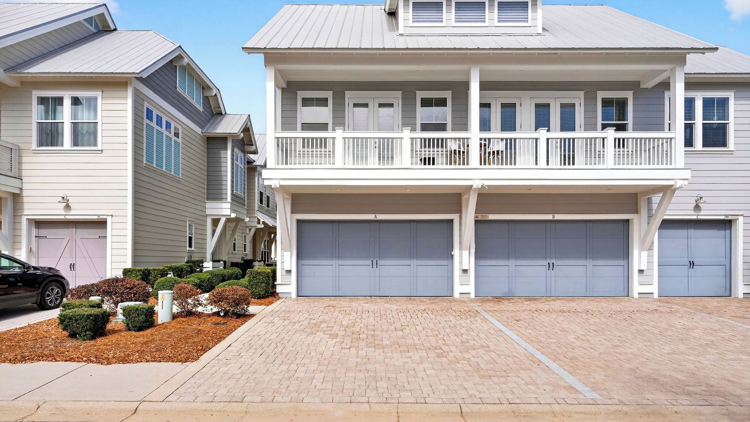 A two-story residential building with a covered front porch, two garages, and a driveway.