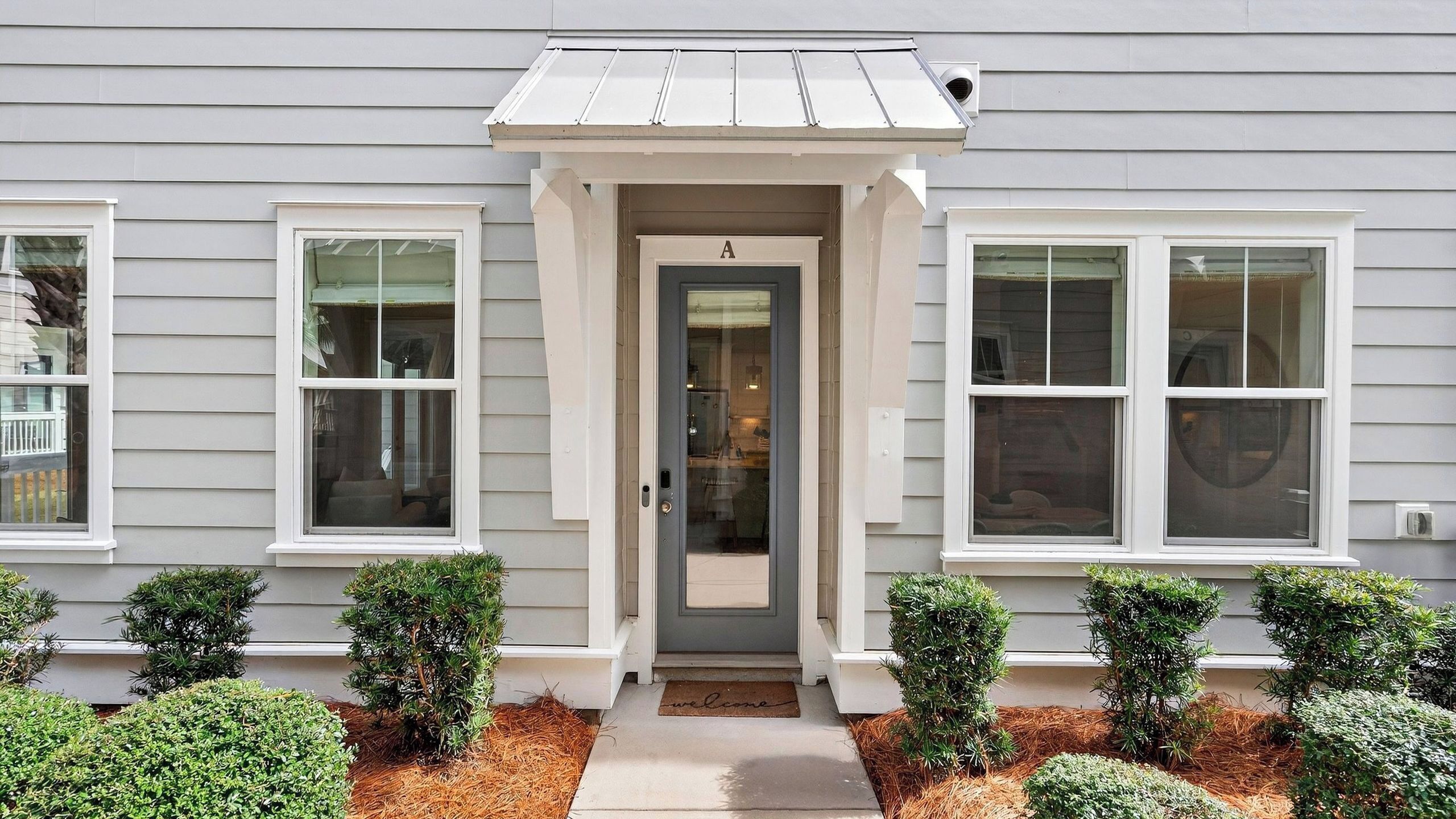 A house with a grey siding exterior, a front door with a small porch, and three windows.