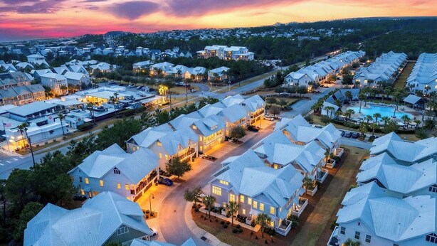 A residential area with houses having unique, angular roofs, a swimming pool, and a well-lit street at dusk.