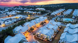 A residential area with houses having unique, angular roofs, a swimming pool, and a well-lit street at dusk.