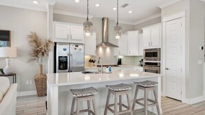 A modern kitchen with white cabinetry, stainless steel appliances, a central island with bar stools, and pendant lighting.