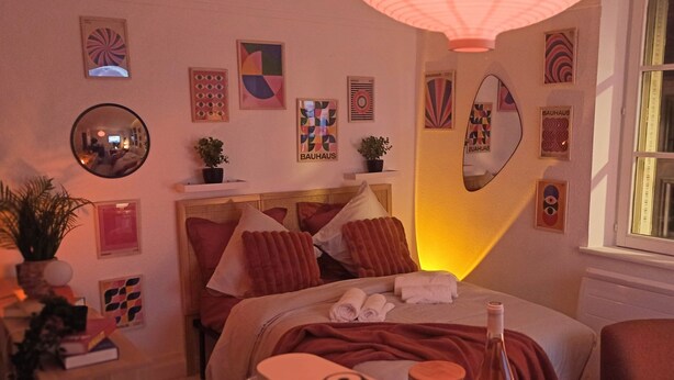A hotel room with a bed, pillows, a bedside table with a bottle, a mirror, and wall art. - Sunset Lovers - WiFi - Netflix - Cosy atmosphere (Nancy)