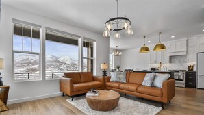 A modern living room with a sectional sofa, a coffee table, and a view of a snowy mountain landscape through large windows. - Jordanelle Ridge Luxury Retreat (Heber City)