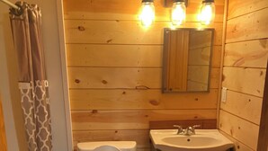 Une petite salle de bain aux murs lambrissés, équipée de toilettes, d’un lavabo et d’un rideau de douche.