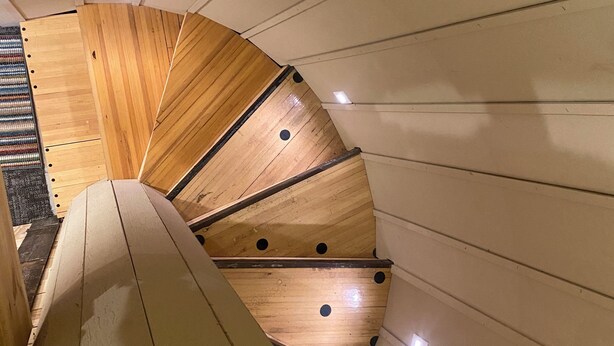 Un escalier en colimaçon avec des marches en bois et un mur de couleur beige.