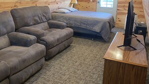 Une chambre mansardée chaleureuse avec un plafond en pente en bois, un lit, un canapé, un bureau avec un ordinateur et une fenêtre.