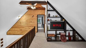 Un escalier avec des finitions en bois, un ventilateur de plafond et une étagère ornée de divers objets décoratifs, ainsi qu’un logo Netflix.