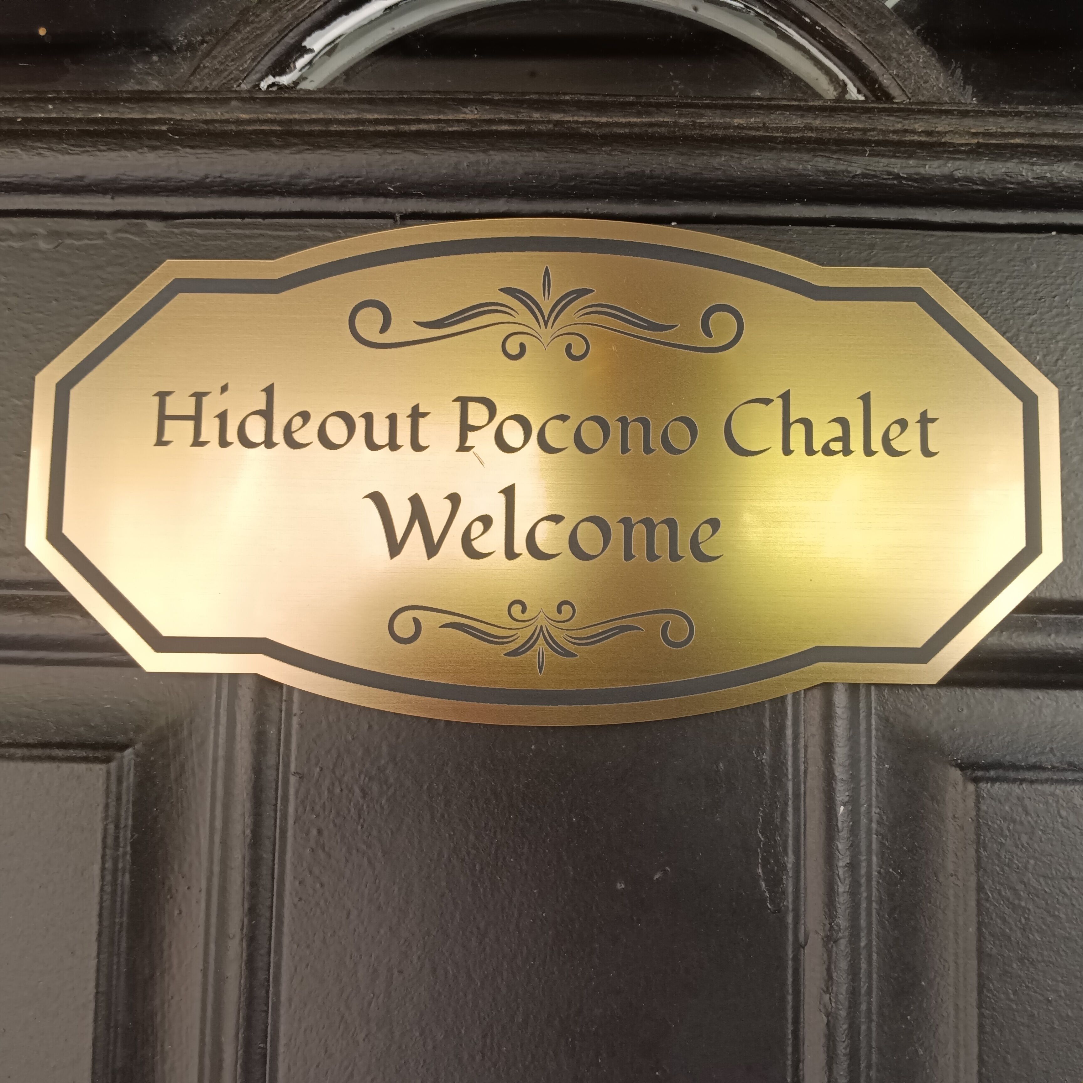 A brass welcome sign with the text "Hideout Pocono Chalet Welcome".
