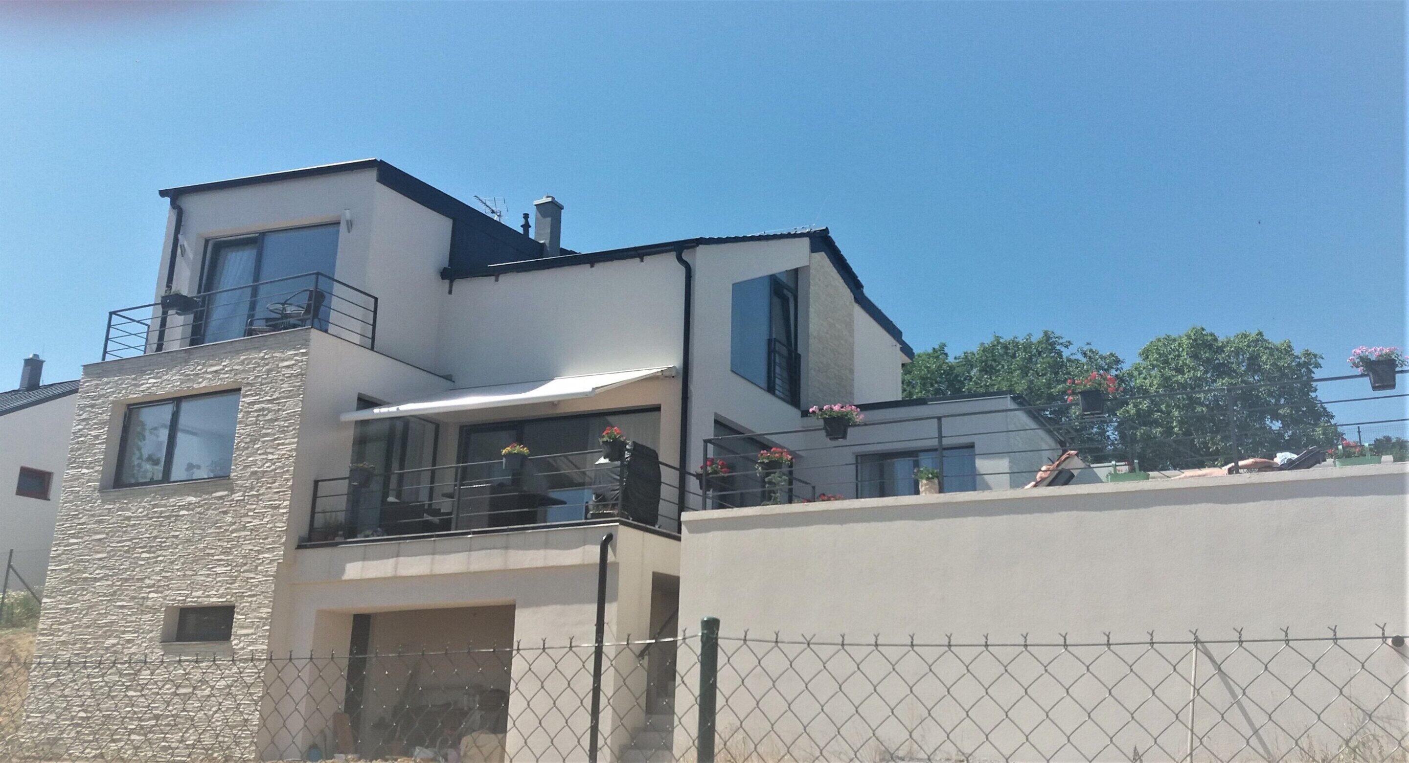 Ein modernes, zweistöckiges Haus mit Naturstein-Fassade, großen Fenstern und einem Balkon mit Topfpflanzen.