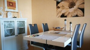 Een eetgedeelte met een witte tafel, vier stoelen, een kast met glazen deuren en een bloemversiering aan de muur.