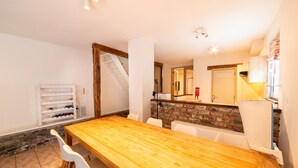 Een eetgedeelte met een houten tafel en witte stoelen, een wijnrek en een bakstenen muur.