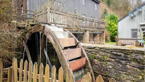 Een rustieke watermolen met een houten omheining op de voorgrond.