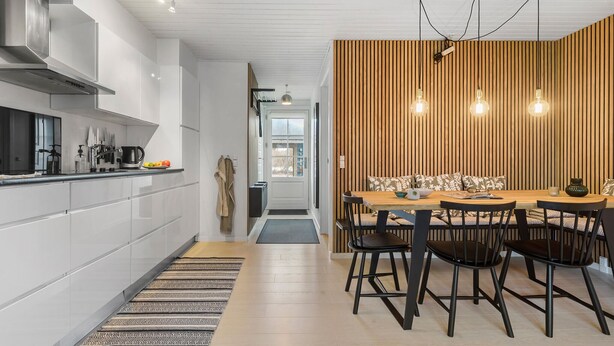 A modern kitchen with white cabinetry, a stainless steel range hood, and a dining area with a wooden accent wall and pendant lights. - Gorgeous apartment in Vestervig (Vestervig)