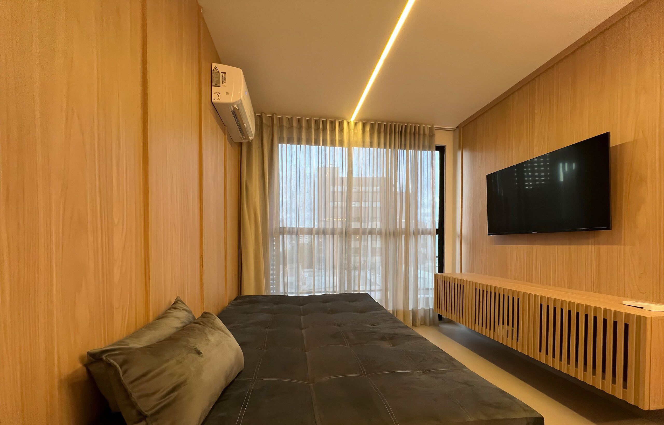 Una camera moderna con un letto, una TV a parete e una finestra con tende.