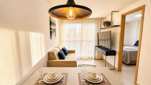 A modern living room with a sofa, a dining table set for two, and a TV stand. - Oceânica Cabo Branco (João Pessoa)