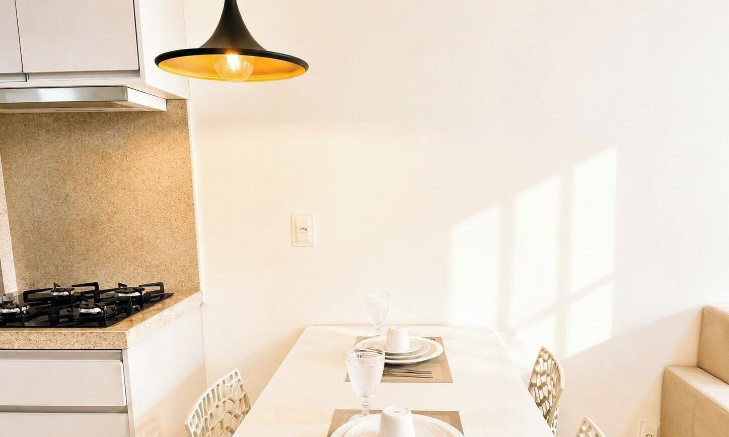 A dining area with a table set for two, a gas stove, and a pendant light.