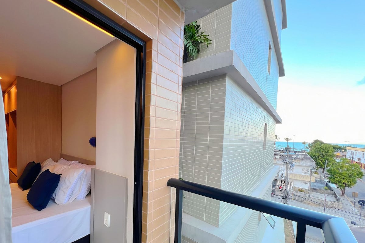 A balcony with a bed, a potted plant, and a view of the cityscape.