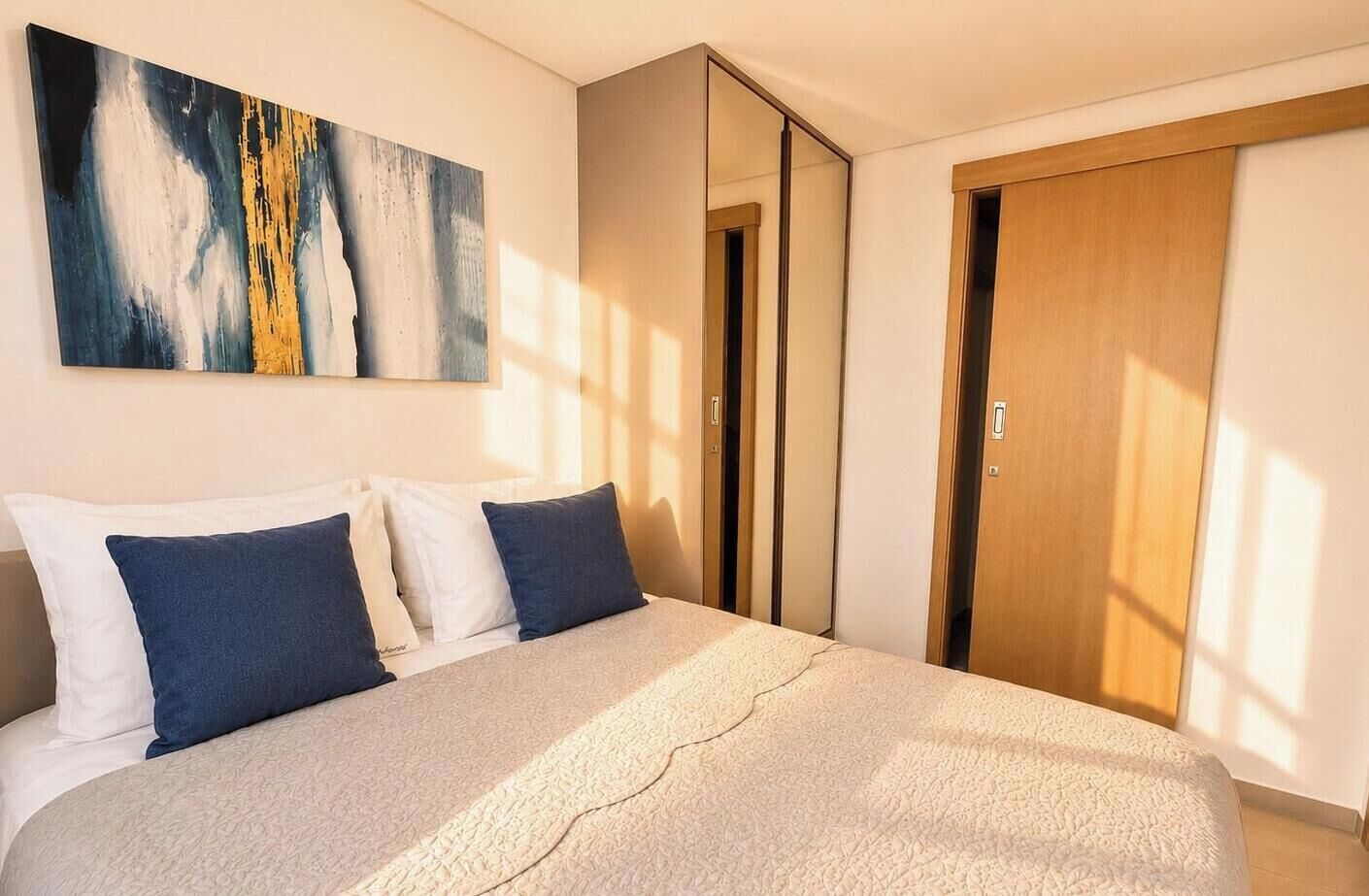 Een slaapkamer met een bed, kussens, een schilderij en een kledingkast.