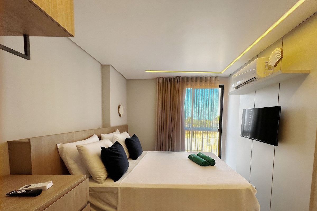 A hotel room with a bed, a TV, a bedside table, and a window with curtains.
